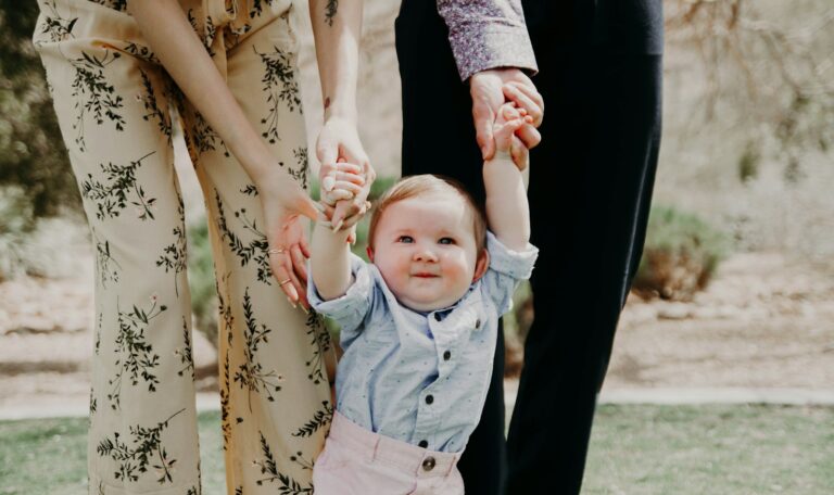 man and woman holding hand of toddler walking on grass field
